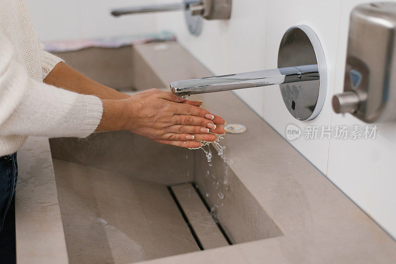 Women's hands under the water jet from the mixer. A middle-aged woman washes her hands in the bathroom